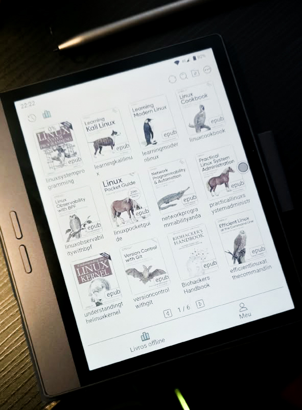 A Bigme B7 e-reader displays a library of Linux and technology e-books, including titles on Kali Linux, Linux administration, Git, networking, and biohacking, photographed at an angle on a dark desk.